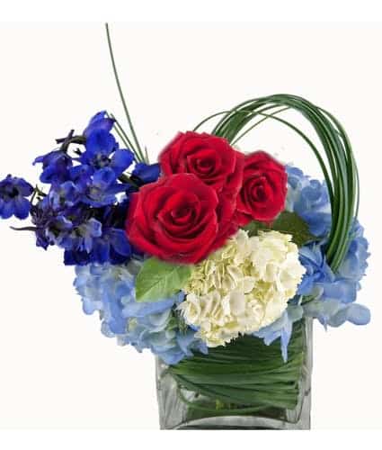 Red roses, blue hydrangea, white carnations in square glass cube.
