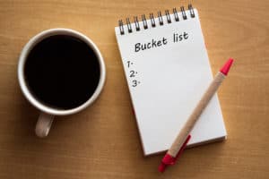 Bucket list in white notebook, coffee, and red pen 